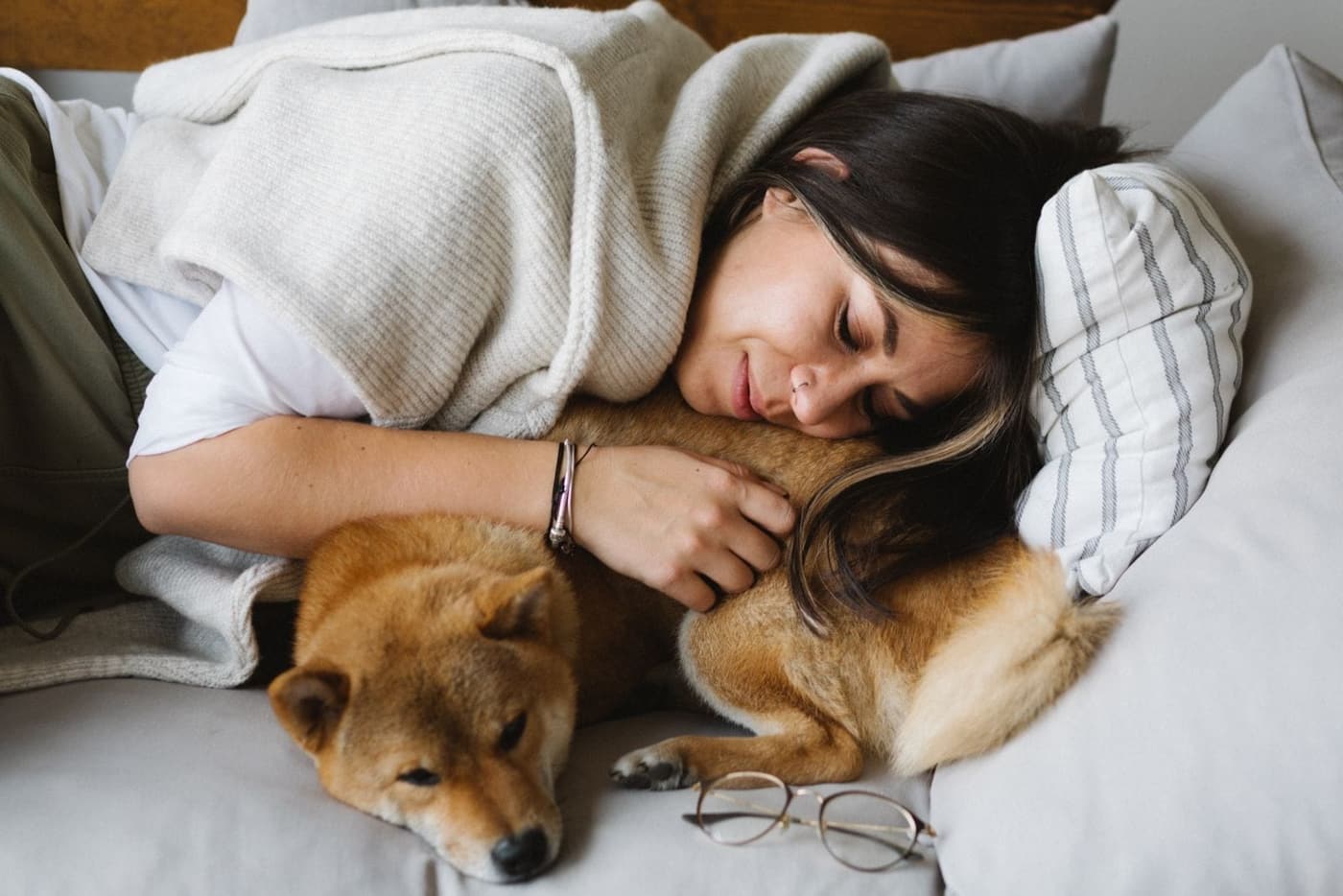 A woman lying on a bed with her arm around a sleeping Shiba Inu